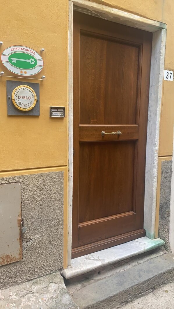 A wooden door with a brass handle, a number '37' on the wall, and two plaques with text and numbers. - OBLO' PORTOVENERE GUESTHOUSE (Portovenere)