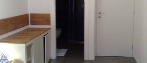 A bedroom with a bed, a desk, a wardrobe, and a shower area.