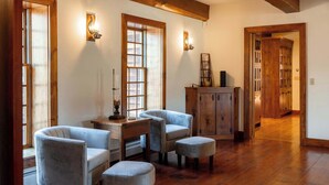 A room with a wooden floor, a desk with a lamp, two armchairs, and a cabinet.