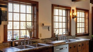 A kitchen with two sinks, wooden cabinets, and large windows.