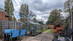 Une terrasse avec une table et des chaises, une serre et une clôture en bois.