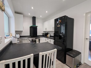 A modern kitchen with a black refrigerator, white cabinets, and a black countertop. - The Pollard Home | Acocks Green (Birmingham)