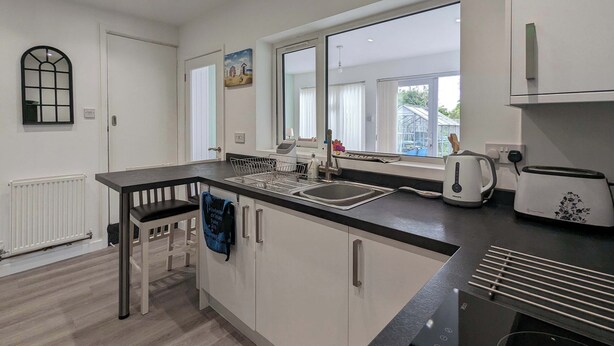 Une cuisine moderne avec un plan de travail noir, des meubles blancs, une fenêtre et une vue sur la verdure à l’extérieur.