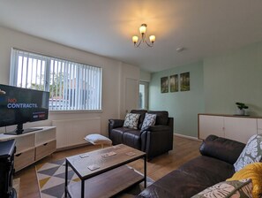 A living room with a sofa, armchair, coffee table, and a television displaying a message. - The Pollard Home | Acocks Green (Birmingham)