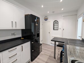 A modern kitchen with white cabinets, a black refrigerator, and a dining area with a metal rack. - The Pollard Home | Acocks Green (Birmingham)
