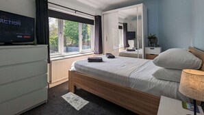 Une chambre à coucher avec un lit, une télévision, une fenêtre, un miroir et une table de chevet.
