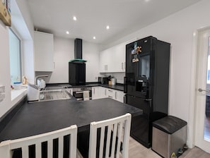 A modern kitchen with a black refrigerator, white cabinets, and a black countertop. - The Pollard Home | Acocks Green (Birmingham)