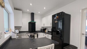 Une cuisine moderne avec des meubles blancs, un réfrigérateur noir, un four en acier inoxydable et un plan de travail noir.