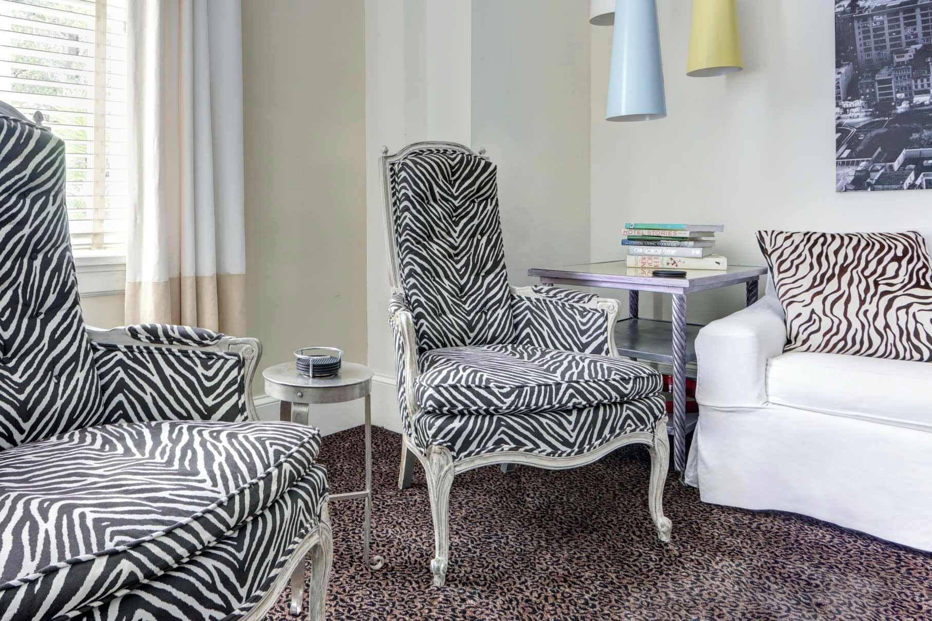 A room with a zebra-patterned chair, a white sofa, a small table with books, and a cityscape painting.