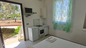 Een compacte hotelkamer met kitchenette, een bed, een televisie en een raam met gordijn.