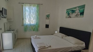 Een slaapkamer met een bed, een televisie, een koelkast en een schilderij aan de muur.