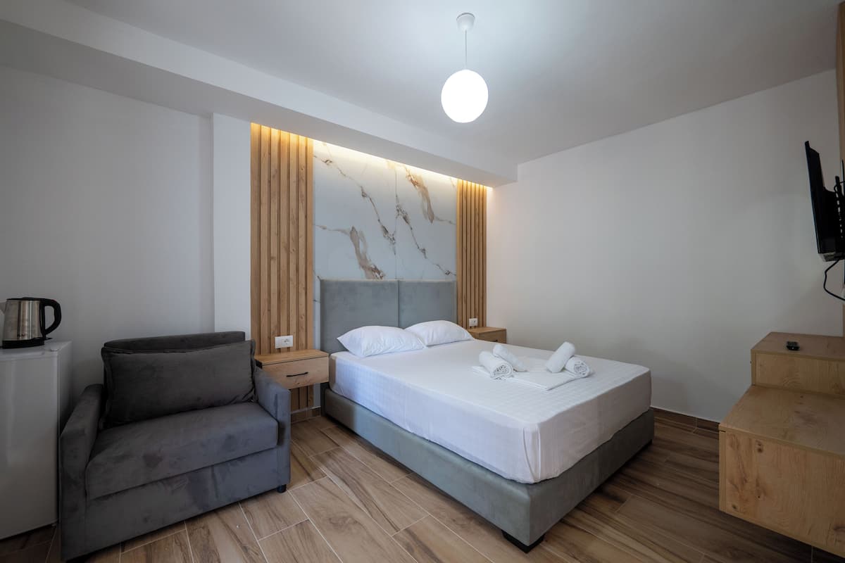 Una habitación de hotel moderna con cama, sofá, mesita de noche de madera y cafetera.