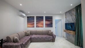 A modern living room with a sectional sofa, a flat-screen TV, and abstract wall art. - Vila Sefedin (Ksamil)