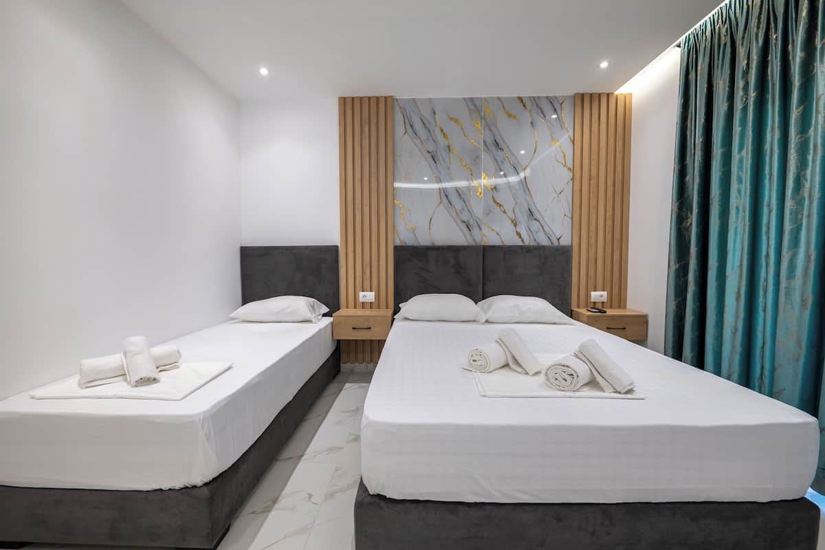 Habitación de hotel con dos camas individuales, una pared de mármol, paneles de madera y una cortina color aguamarina.