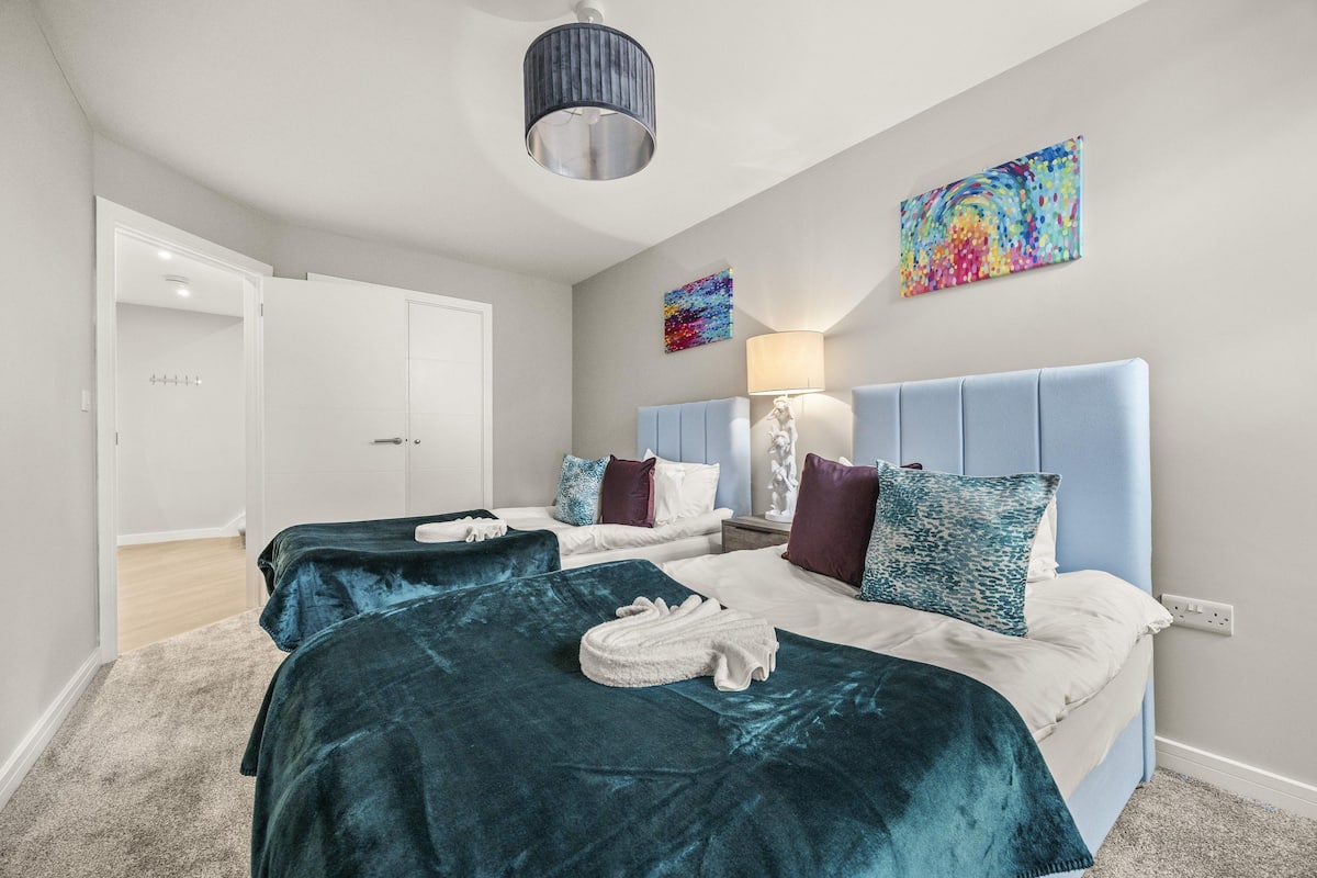 A hotel room with two beds, a large window, a ceiling light, and a painting on the wall.