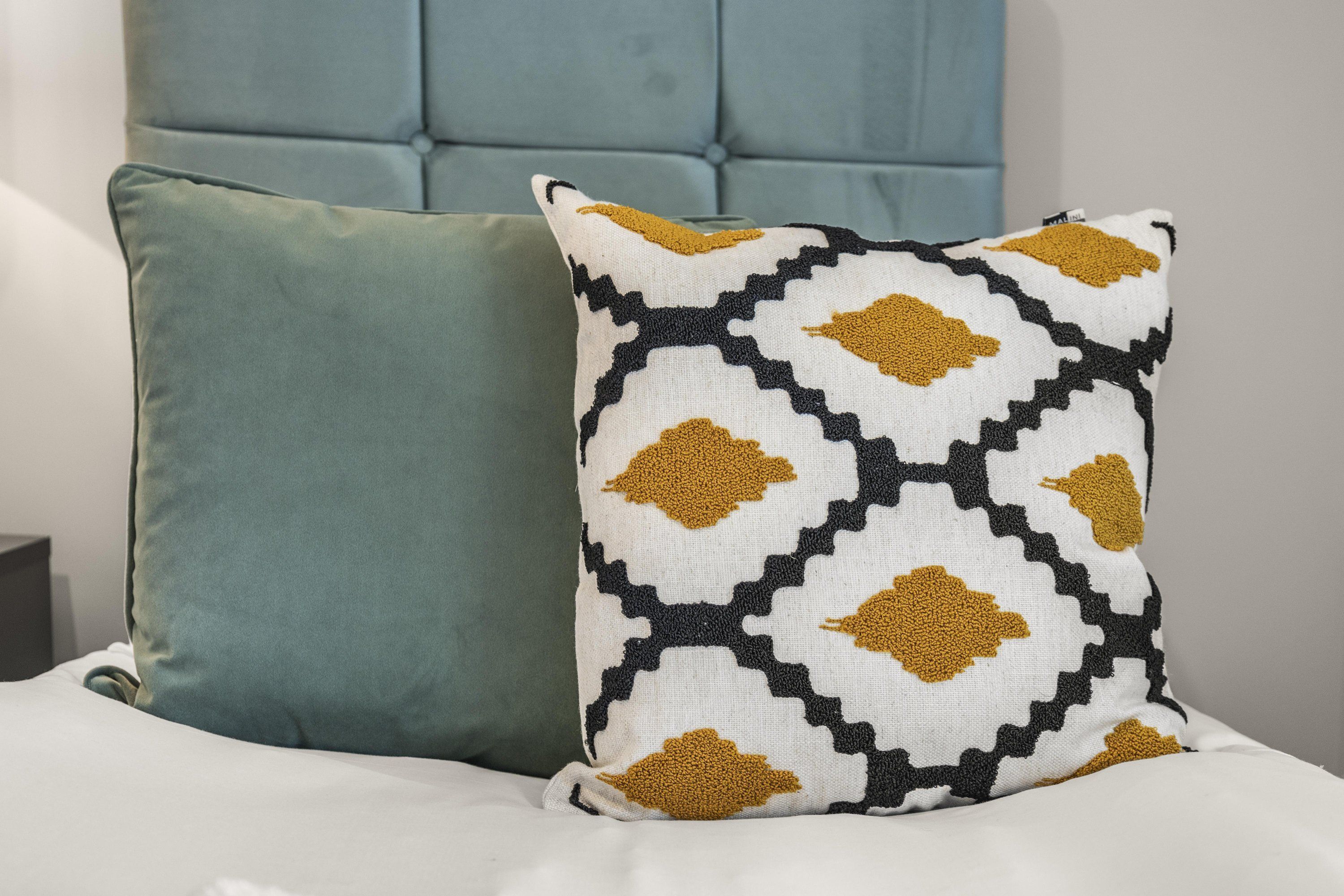 A bed with two pillows, one plain and one patterned.