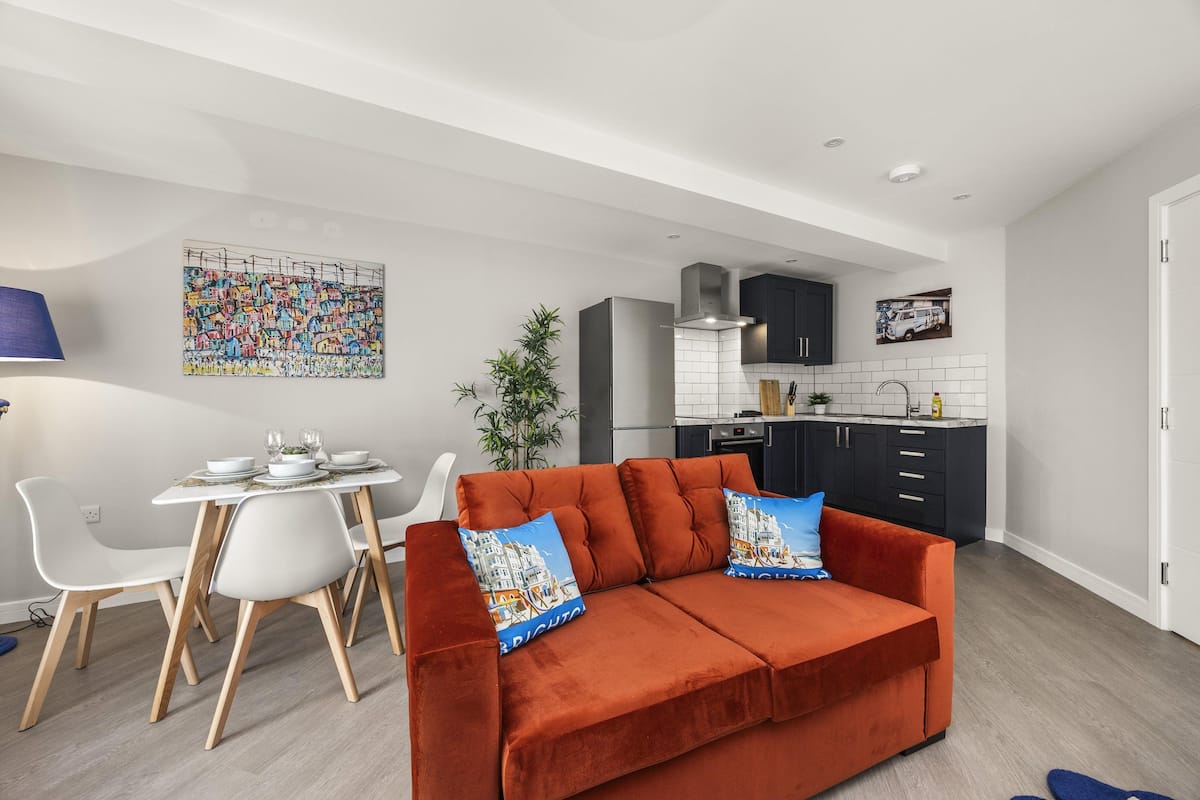 A modern living room with a red sofa, white dining chairs, and a kitchen in the background.