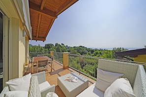 A balcony with wicker furniture, a table, and chairs, overlooking a lush landscape.