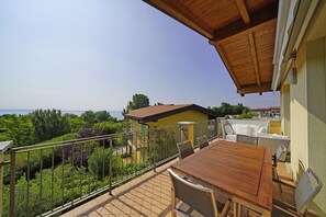 Un balcon avec une table et des chaises en bois, une vue sur la mer et un jardin.