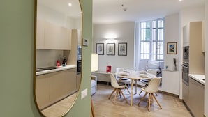 A modern kitchen with white cabinets, a dining area with a round table and chairs, and a large mirror. - Brignole Refined Home by Wonderful Italy (Genova)