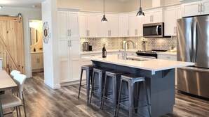 A modern kitchen with white cabinets, a central island with bar stools, stainless steel appliances, and pendant lighting.