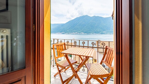 Un balcón con mesa y sillas de madera, con vista a un paisaje montañoso y un cuerpo de agua.