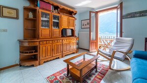 Una sala de estar con un mueble de madera, una mesa de centro de vidrio, un sofá azul y un balcón con vistas a montañas.