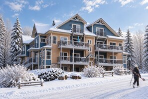 A multi-story hotel with balconies, snow-covered surroundings, and a person skiing.