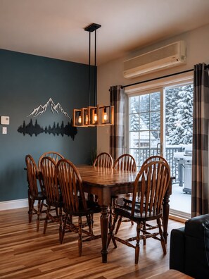 A dining area with a wooden table and chairs, a mountain mural on the wall, and a view of a snowy landscape through the window.