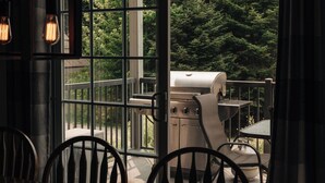 En balkon med grill, stole og udsigt til et skovområde.