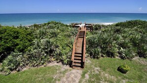Un sentier en bois mène à une plage bordée de part et d’autre d’une végétation tropicale luxuriante.