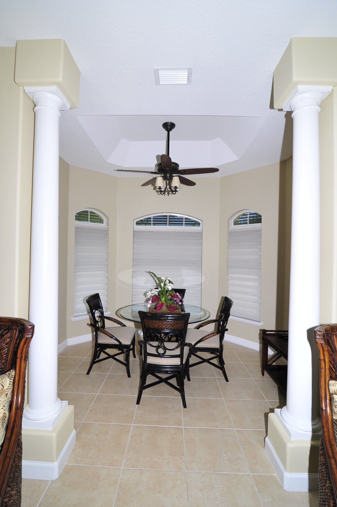 A dining area with a round table, four chairs, a ceiling fan, and a decorative vase.