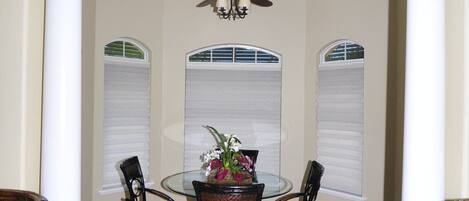 A dining area with a round table, four chairs, a ceiling fan, and a decorative vase.