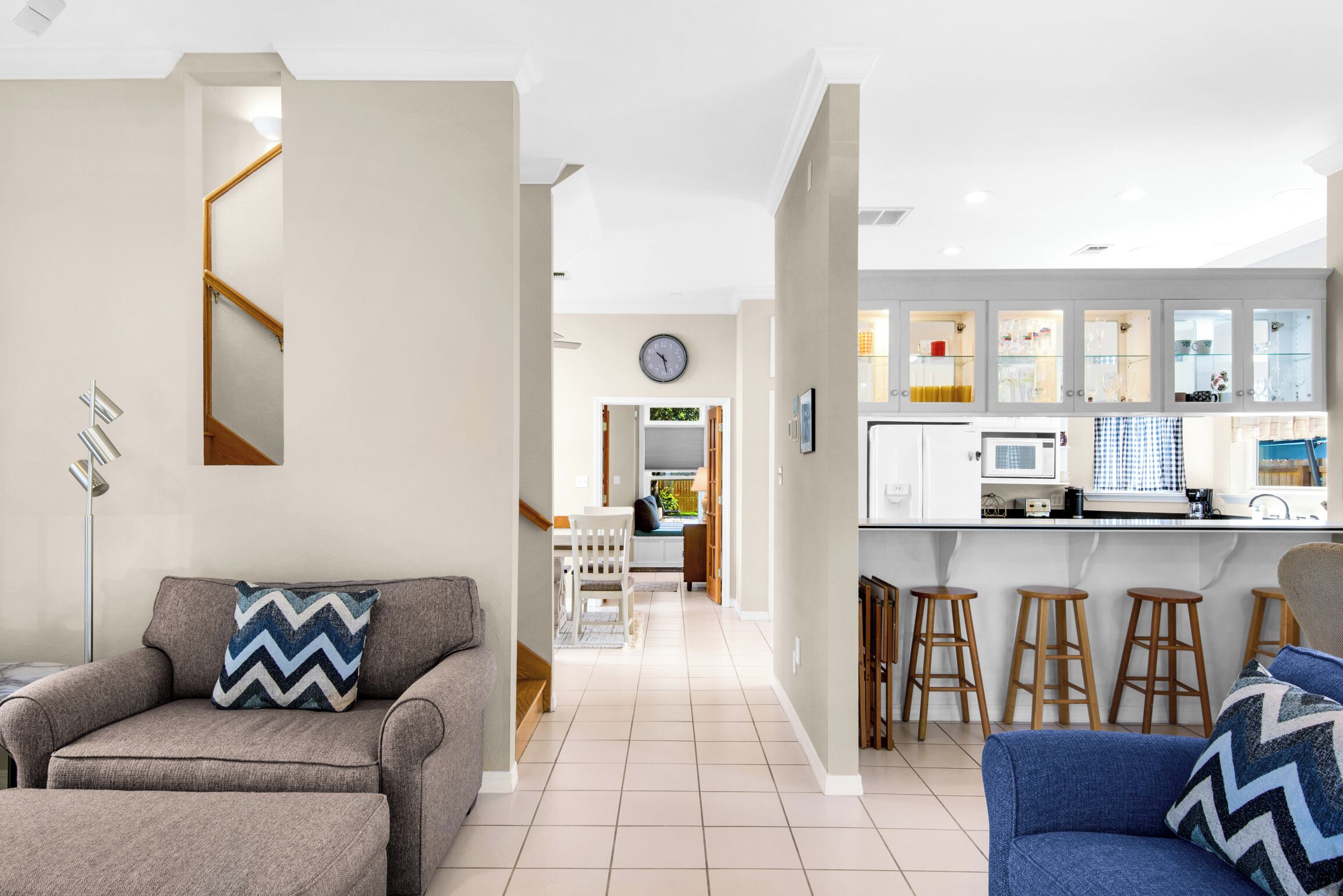 A modern living room with a sofa, a blue armchair, and a dining area with a kitchen in the background.