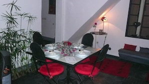 A dining area with a table set for four, surrounded by chairs with red cushions. A small table with a lamp and a vase of flowers is against the wall. - Riad La Parenthese (Marrakech)