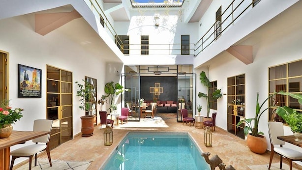 A spacious indoor pool area with a central seating area, surrounded by potted plants and modern furniture. - Riad La Parenthese (Marrakech)