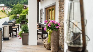 An outdoor seating area with tables and chairs, a large planter with flowers, and a lantern. - Hotel Sendlhof (Waidring)