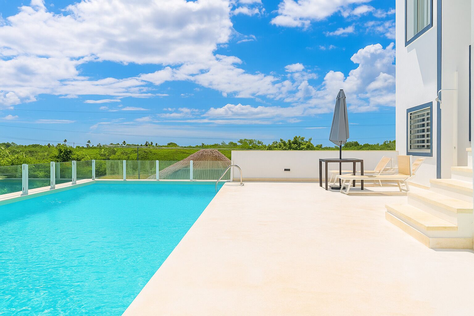 A swimming pool with a clear blue sky and a white building with steps and a table with chairs.
