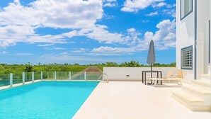 Una piscina con cielo azul despejado y un edificio blanco con escalones y una mesa con sillas.