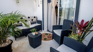 Un espacio de estar al aire libre con muebles de mimbre, plantas en macetas y un ventanal corredero que da a un balcón.