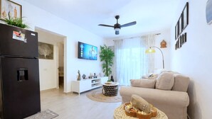 Una sala de estar moderna con un refrigerador negro, un sofá beige, un ventilador de techo y un televisor de pantalla plana.
