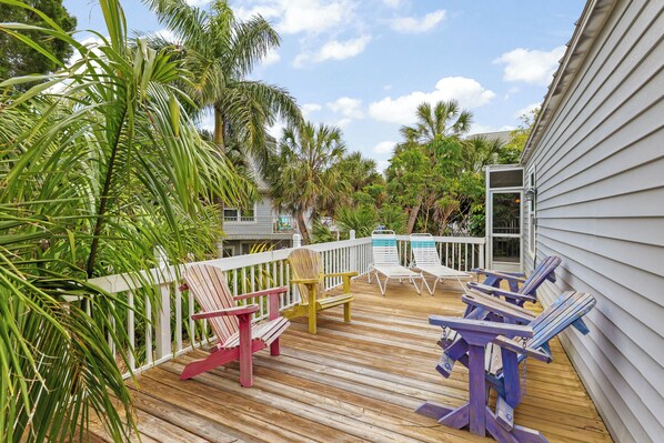 A wooden deck with colorful Adirondack chairs and a pool area.
