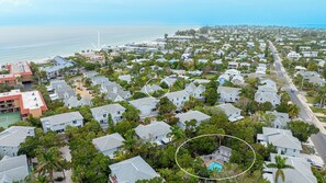 An aerial view of a coastal residential area with houses, a beach, and a wind turbine.