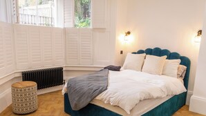 A bedroom with a teal bed, white bedding, and two wall-mounted lights. - Stunning Victorian apartment with garden (London)