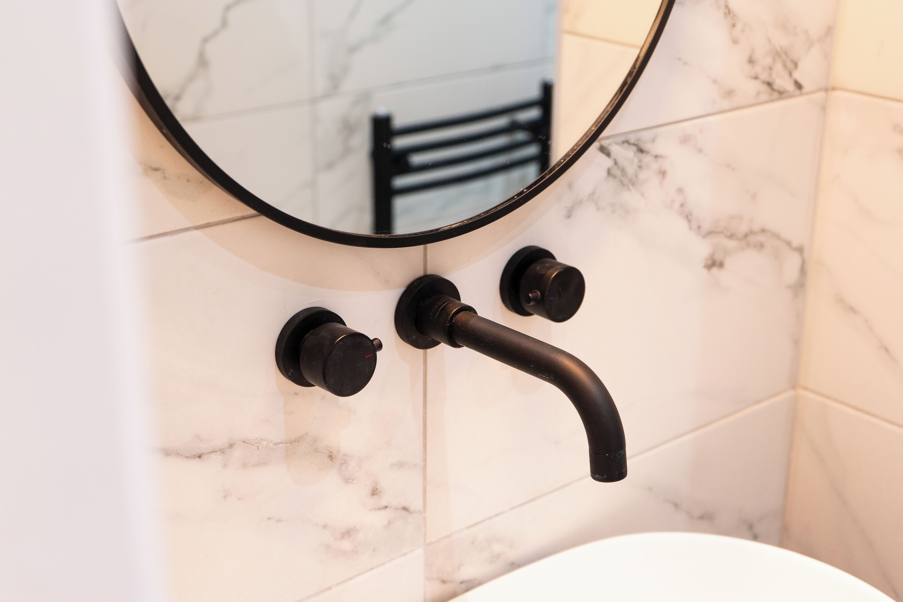 A bathroom with a white marble sink, a black faucet, and a round mirror.