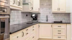 A modern kitchen with white cabinets, a black countertop, and a coffee machine. - Stunning Victorian apartment with garden (London)
