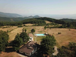 Une propriété rurale dotée d’une piscine, entourée de champs et d’arbres, et offrant une vue sur des collines lointaines.
