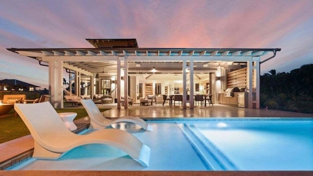 A modern pool area with lounge chairs, a covered patio, and a view of the surrounding landscape. - Hale Honu Kukui'ula By Suite Paradise (Koloa)