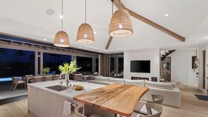A modern kitchen with a wooden island, pendant lighting, and a large dining table. - Hale Honu Kukui'ula By Suite Paradise (Koloa)