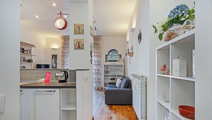 A modern kitchen with white cabinetry, a coffee machine, and a clock. There is a living area with a sofa and a bookshelf. - Cozy Lighthouse Apartment by Wonderful Italy (Santa Margherita Ligure)
